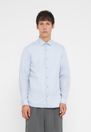 Camisa de botones de manga larga en azul claro con cuello, que presenta una tela texturizada y cierre frontal de botones. Combinada con pantalones grises.