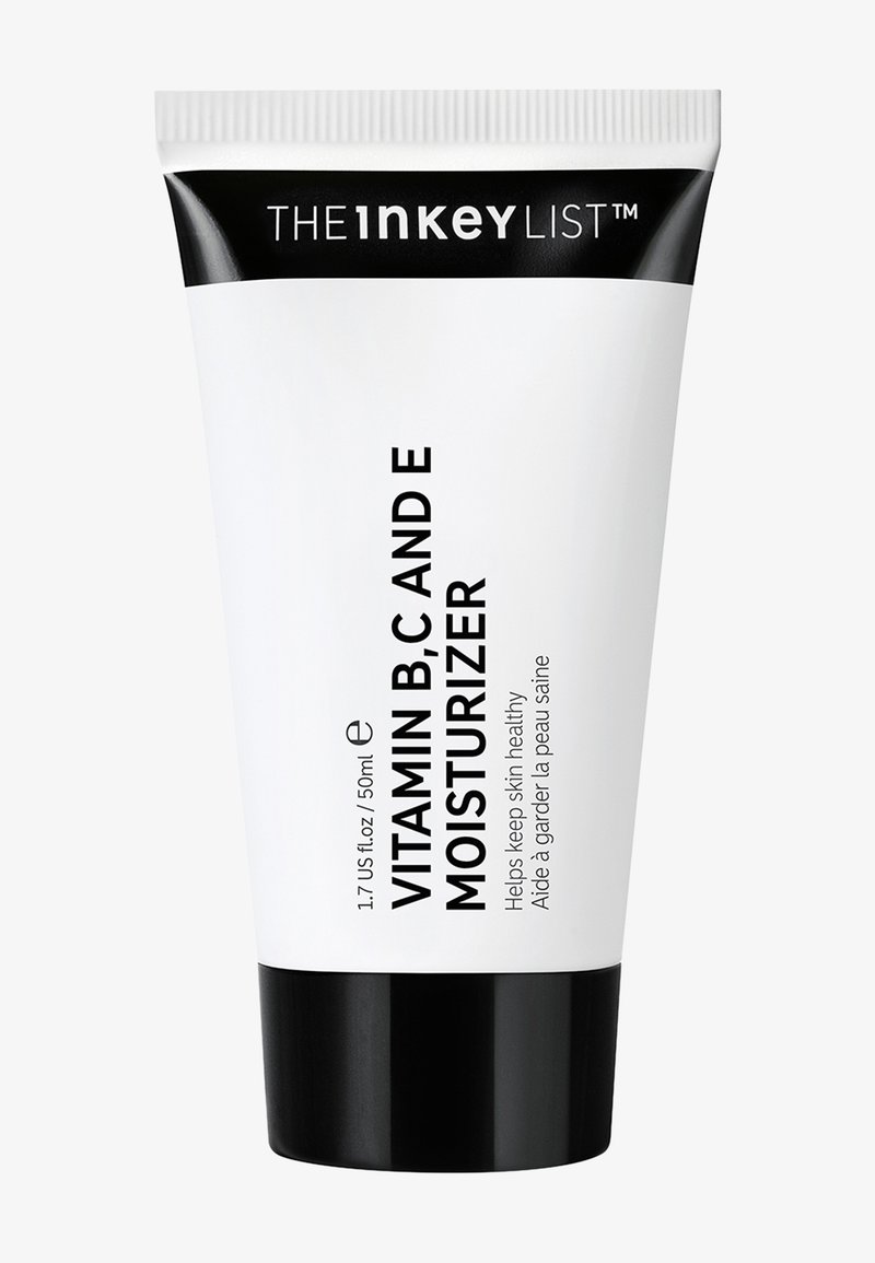 Crème hydratante en tube compressible avec un corps blanc et un fond noir, étiquetée "Vitamines B, C et E", avec une finition mate et un texte noir en gras.
