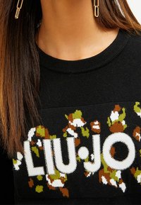 Suéter negro con un patrón floral en colores como verde, marrón y blanco, con el nombre de la marca "LIU.JO" embellecido en blanco y con rhinestones.