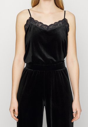 Sort fløjls-camisole med blonder langs udskæringen, med tynde stropper. Blød tekstur og løs pasform. Kombineret med matchende sorte bukser.