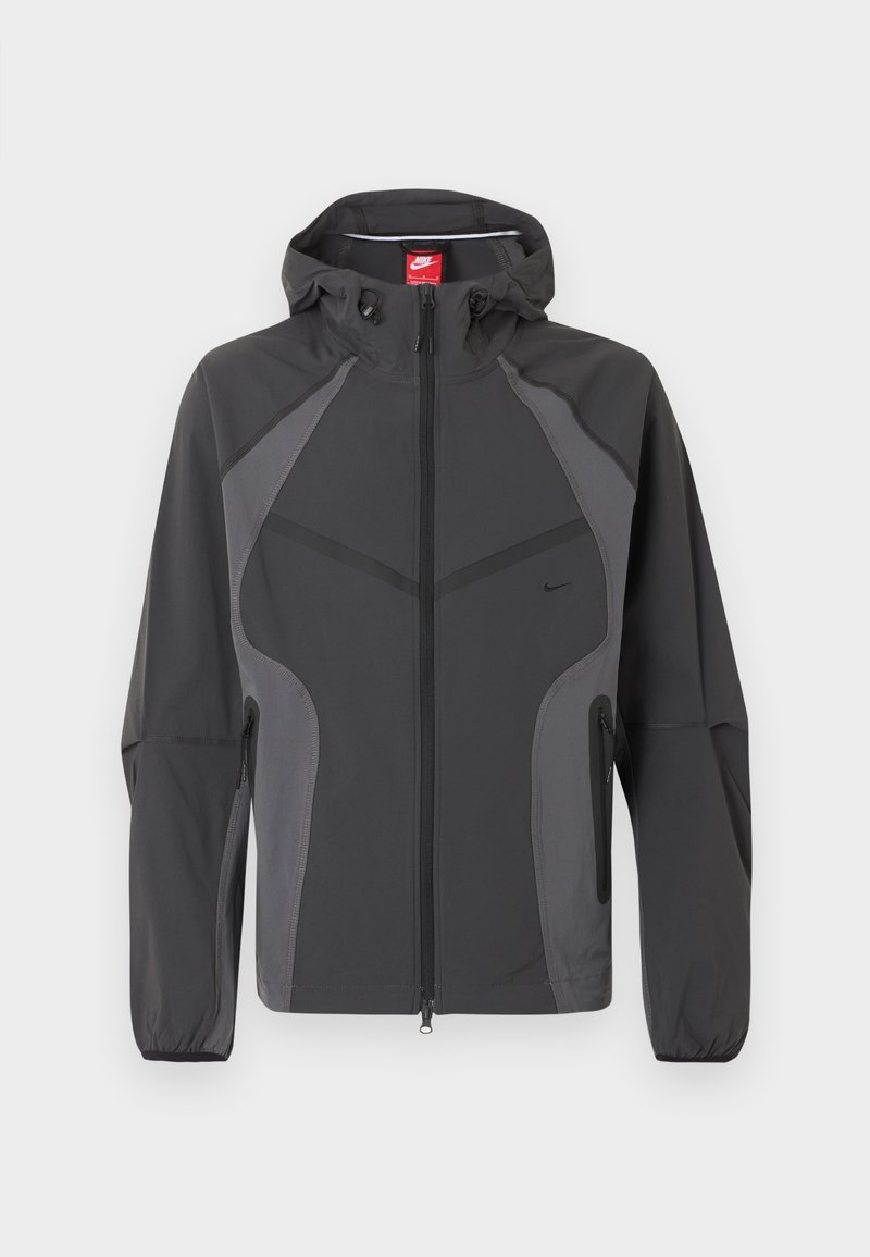 Dunkelgraue Nike Kapuzenjacke mit durchgehendem Frontreißverschluss, seitlichen Reißverschlusstaschen und elastischen Bündchen, dargestellt vor weißem Hintergrund.