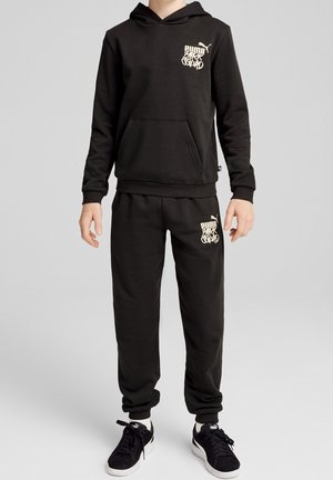 Musta huppari ja joggarihousut pehmeästä kankaasta. Edessä tasku, logodetalji kermaisessa värissä ja resorit hihansuissa. Asun täydentävät tennarit.