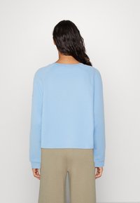 Jasnoniebieska bluza z okrągłym dekoltem, rękawami raglanowymi i ściągaczami, w połączeniu z beżowymi spodniami o szerokich nogawkach. Gładka tekstura.