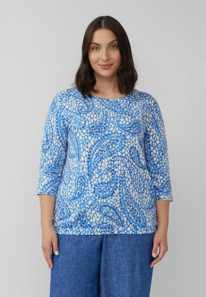 Blauw en crèmekleurig patroon top met driekwartmouwen, met een mix van abstracte vormen en een zachte textuur, gedragen met denim onderstukken.