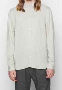 Camicia grigia chiara con bottoni realizzata in cotone, dotata di taschino sul petto, colletto alla francese e maniche lunghe con polsini abbottonati.