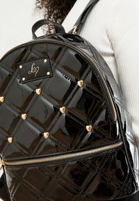 Must mustrikuuri mustrikuur nahaga seljakott, millel on tikitud disain, kuldsed südame aksessuaarid, kuldne lukku ja logotempel, millel on reguleeritavad sangad.