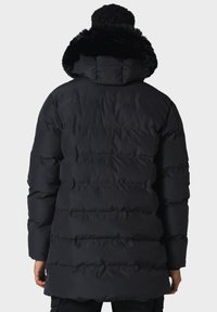 Zwarte donsjas met een capuchon gevoerd met nepbont, doorgestikt ontwerp en een middellange lengte. Glad, glanzend stof met een ontspannen pasvorm.
