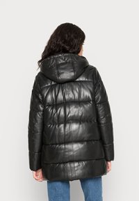 Černá kožená péřová bunda s kapucí, obsahující prošívané části pro izolaci a středně dlouhý střih. Hladký, lesklý povrch s minimálními detaily.