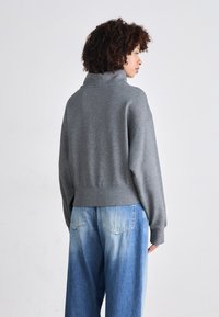Grauer übergroßer Pullover mit hohem Kragen, geripptem Saum und überschnittenen Schultern, kombiniert mit hellblauen Ombre-weit geschnittenen Jeans.