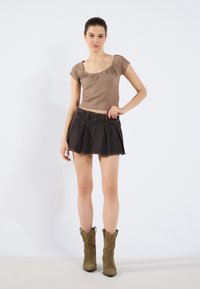 Brązowy żeberkowany crop top z krótkimi rękawami, w zestawie z czarną plisowaną mini spódnicą z denimu i zielonymi zamszowymi botkami sięgającymi kostki.