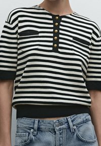 Randig stickad topp i svart och vitt, med rund hals, korta ärmar, fem guldknappar och en framficka.