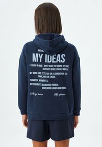 Sudadera azul marino en una suave mezcla de algodón, con grandes letras blancas en la parte posterior que contienen frases inspiradoras y capucha con cordón.