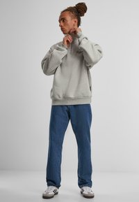 Sudadera de forro polar gris con cuello de media cremallera, combinada con jeans de mezclilla azules y zapatillas blancas con acentos marrones y rayas negras.