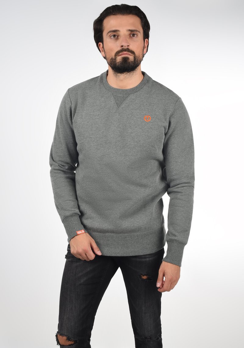 Gray sweatshirt with a crew neck, knit texture, and an orange logo on the chest. Worn with distressed black jeans.