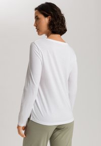 Camisa blanca de manga larga con escote redondeado, textura suave y aberturas laterales, combinada con pantalones verde claro.