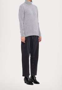 Pull à col roulé gris en tricot avec poignets côtelés, associé à un jean denim noir ample et des bottines noires à bouts pointus. Design simple et texturé.