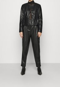 Czarna skórzana kurtka z okrągłym kołnierzem i zapięciem na napy, w połączeniu z dopasowanymi, luźnymi spodniami oraz czarnymi, wąskimi botkami za kostkę.