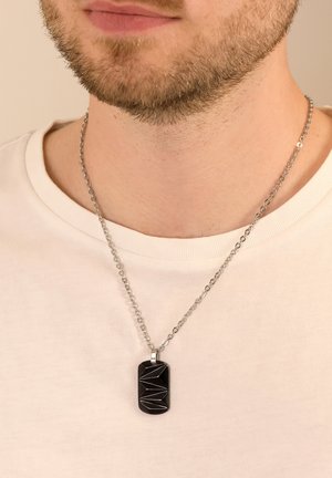 Silberne Kettenhalskette mit einem rechteckigen schwarzen Anhänger, der ein geometrisches Schnittdesign aufweist. Der Anhänger ist poliert und hat eine strukturierte Oberfläche.