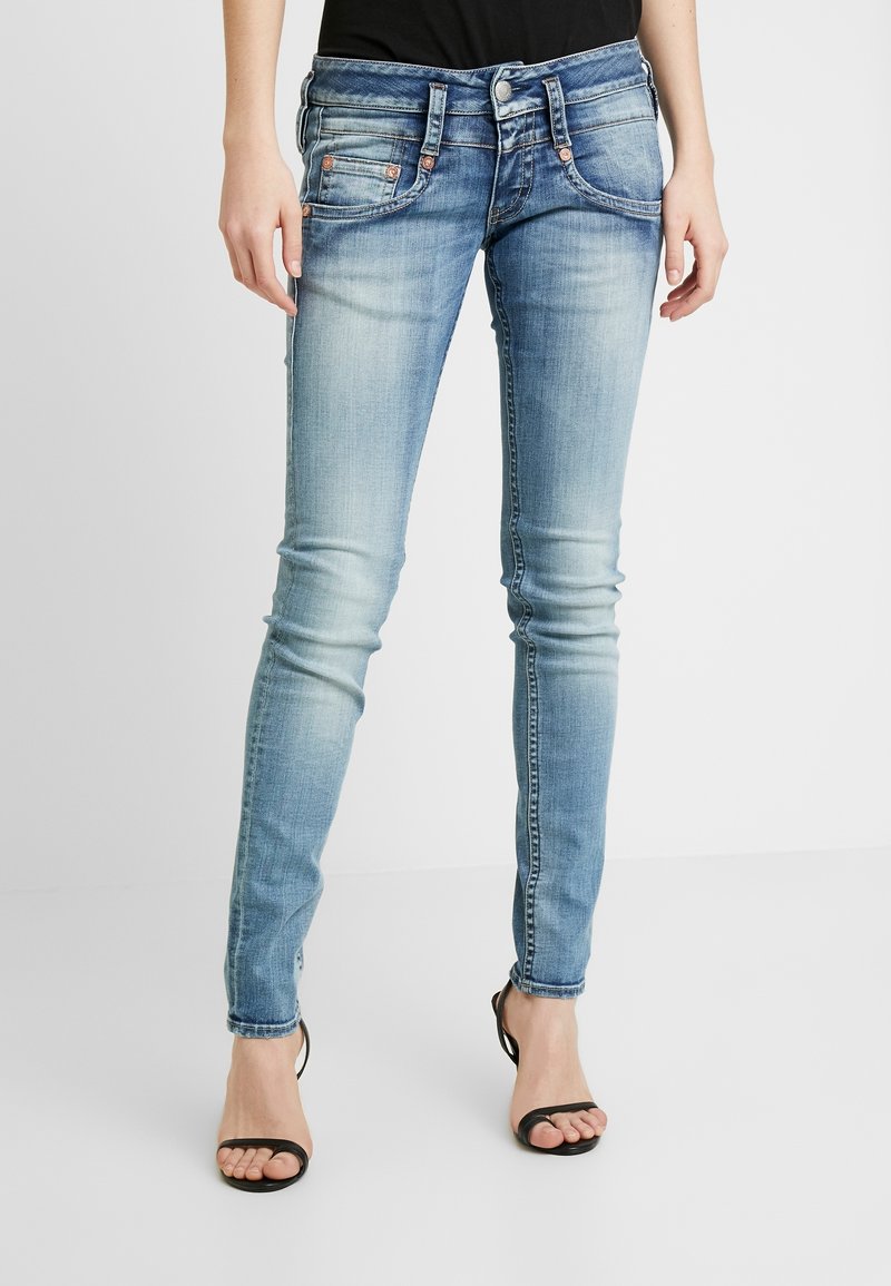 Falnad blå denim skinny jeans med fem fickor, metalliska nitar och en något sliten yta. Har en knapp- och dragkedjestängning.
