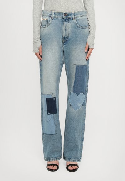 Light blue denim jeans with various patch designs in darker shades, featuring heart-shaped and rectangular patches on both legs.