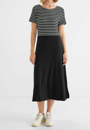 Gestreepte zwart-witte top met korte mouwen, overgaand in een effen zwarte rok, gedragen met witte sneakers; zachte stof, relaxed fit.