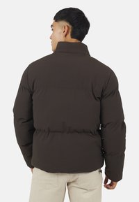 Giacca a vento marrone con colletto alto e tessuto testurizzato. Presenta una silhouette aderente e cuciture visibili sul retro.