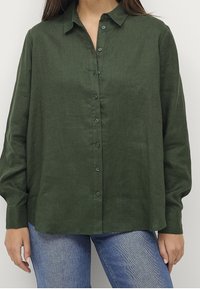 Camicia button-up in lino verde scuro con colletto, maniche lunghe e una vestibilità rilassata. Presenta bottoni sul davanti e un tessuto texturizzato.