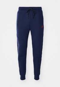 Mørkeblå sweatpants med snoreliv, buede sømme og sidelommer. Har et lille rødt logo på den øverste venstre ben.
