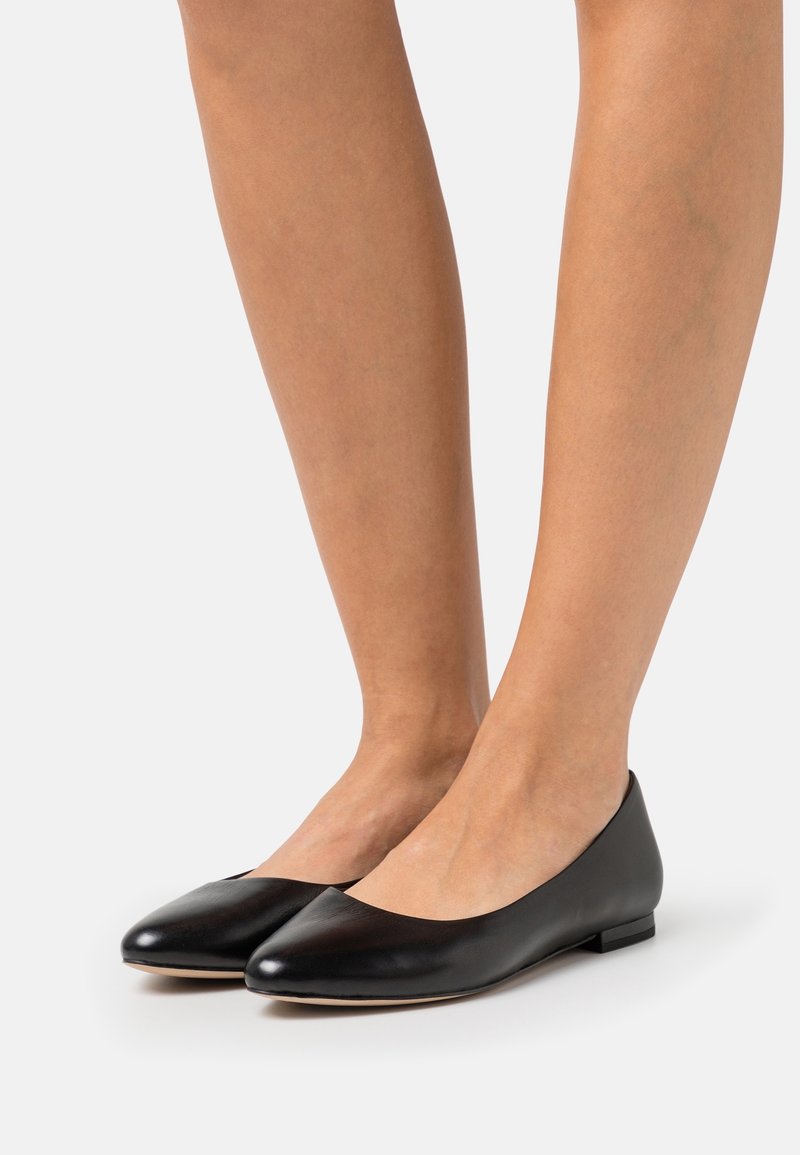 Ballerines en cuir noir avec bout pointu, petit talon et texture lisse, présentant un design minimaliste sans ferrures visibles.