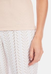 Light beige fitted top with a smooth texture features a subtle logo. White patterned leggings with diagonal lines and dots.