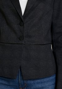 Dark gray blazer featuring a subtle textured pattern, two buttons, and a tailored fit, complemented by a sleek lapel and vented hem.