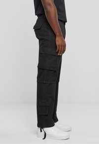 Pantalons cargo noirs en tissu durable, dotés de multiples poches, d'une coupe ample et associés à des baskets blanches.