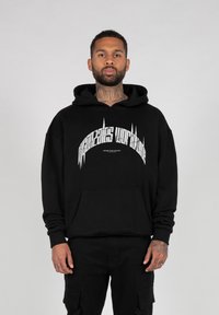 Svart hettegenser laget av tykk stoff, med en fremtredende hvit grafisk utskrift i buet design over brystet. Myk tekstur, frontlomme.