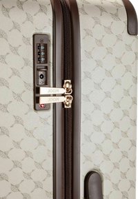 Hardcase koffer in lichtcrème met een subtiele patroonstructuur, voorzien van een dubbele ritssluiting, combinatiebeugel en gouden accenten.