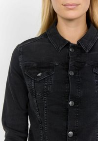 Svart denimjacka med knappslå framtill, två bröstfickor och klassisk krage. Har silverknappar och en mjuk textur.