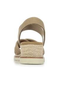 Sandalia de esparto beige con un talón de yute tejido, una amplia correa de tela en el tobillo y una plantilla texturizada para mayor comodidad. Suela plana con un sutil acento.