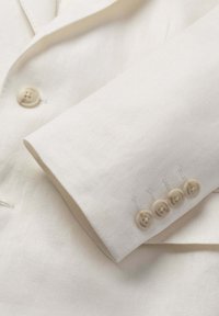 Hvid tekstureret blazerærme med fire beige knapper og matchende knap foran, alle mærket "Hackett London."