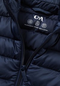 Granatowa pikowana kurtka z rozpiętym zamkiem, na którym widnieje etykieta z informacjami o materiałach pochodzących z recyklingu, lekkiej wadze, możliwościach prania w pralce oraz logo C&A.