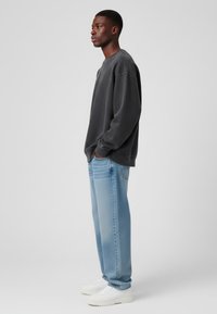 Sudadera oversized de color gris oscuro, jeans relajados de color azul claro y zapatillas blancas. La vista lateral muestra un ajuste casual y una textura de tela suave.