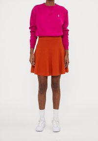 Ljusstark rosa sweatshirt med rund hals och vitt logotyp, kombinerad med en luftig orange kjol. Vita sneakers och knälånga strumpor kompletterar outfiten.