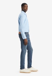 Cămașă bleu deschis cu butoni, blugi din denim și pantofi sport albi. Cămașa are guler și mâneci lungi; blugii sunt mulați și ușor decolorați.