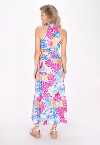 Rochie maxi cu guler halter, având un model floral tropical colorat în roz, violet și albastru pe un fundal roz deschis.