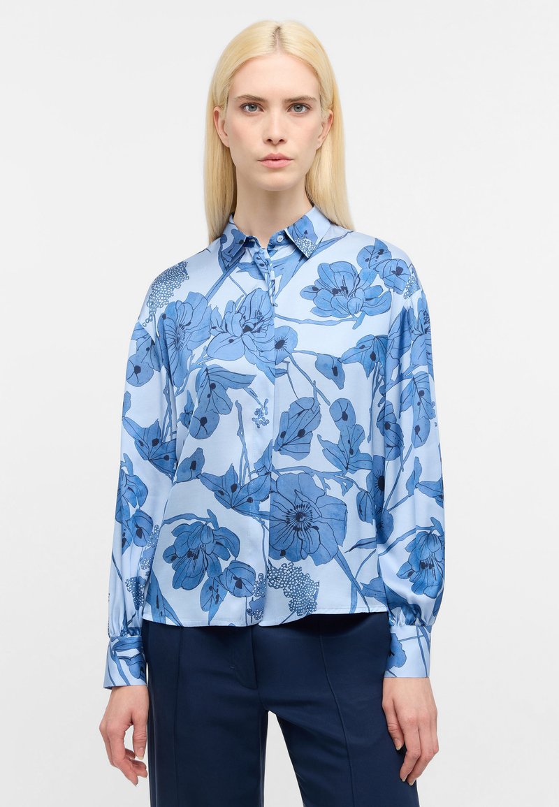 Blusa a fiori blu realizzata in tessuto morbido, con colletto, chiusura a bottoni, maniche lunghe e una vestibilità leggermente rilassata.