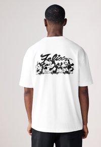 T-shirt en coton blanc avec un graphisme noir de Félix le Chat en train de faire du skateboard, avec le nom "Félix" stylisé au-dessus de l'illustration.