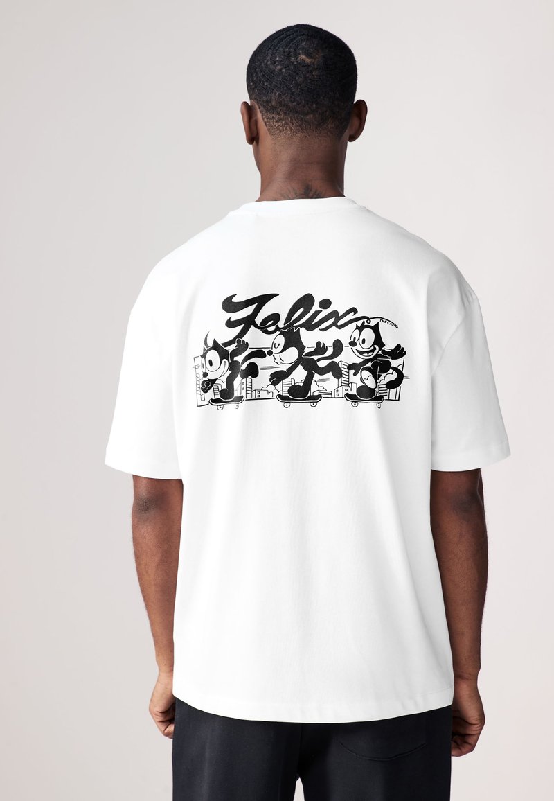 T-shirt en coton blanc avec un graphisme noir de Félix le Chat en train de faire du skateboard, avec le nom "Félix" stylisé au-dessus de l'illustration.