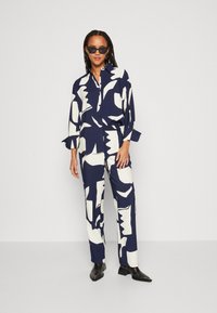 Navy and cream patterned two-piece outfit with a button-up shirt and wide-leg pants; made of smooth fabric, featuring long sleeves and a relaxed fit.