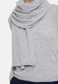 Lysegrå strikket skjerf, myk tekstur, drapert løst, med frynsete ender. Kombinert med en matchende lysegrå genser.