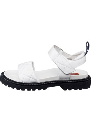 Hvide sandaler med quiltet læderoverdel, justerbar ankelrem og tykk sort gummisål. Har en pull tab på hælen.