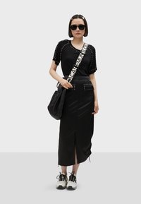 Černý outfit zahrnující tričko se zdobením, sukně s vysokým pasem a kapsami a šněrovací tenisky. Součástí je i ramenní taška.