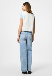 Vitt vadderat väst, kort längd, kombinerat med ljusblå t-shirt och högmidjade ljusa jeans. Svarta stövlar fulländar looken.